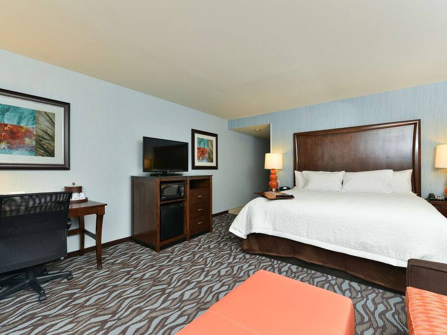 A hotel room with a bed, desk, chair, television, and artwork on the wall.