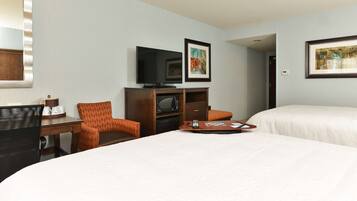 A hotel room with two beds, a desk with a chair, a television, and framed artwork on the wall.