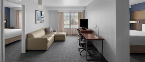 A modern hotel room with a bed, a sofa, a desk, and a TV.