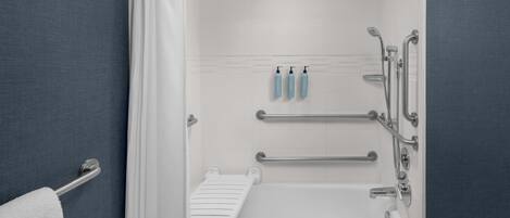 A modern bathroom with a bathtub, shower, and handrails.
