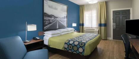Una habitación de hotel con una cama, un escritorio, una silla, una lámpara, un televisor y un cuadro en la pared.