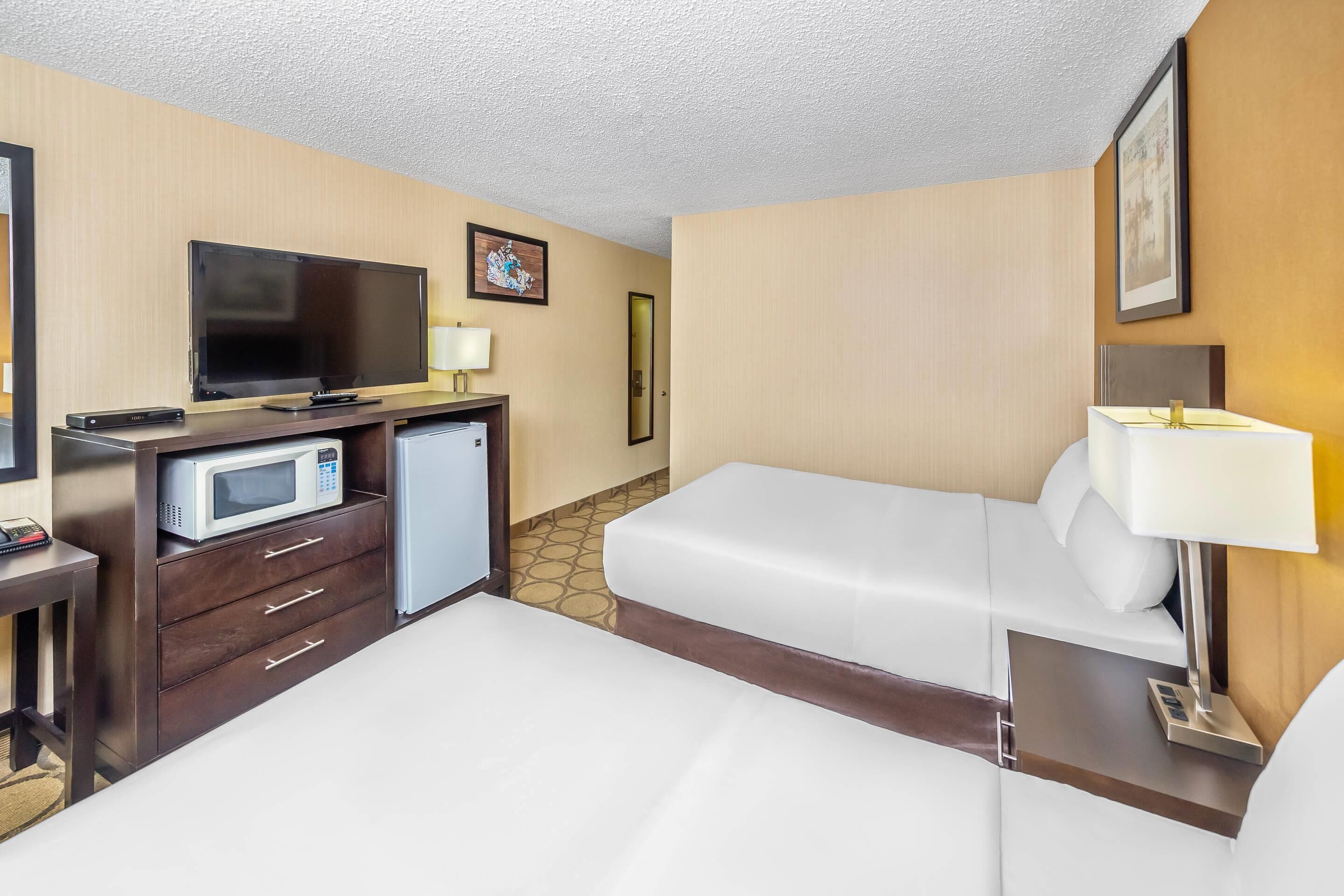 A hotel room with a bed, a desk with a microwave, a television, and a small refrigerator.
