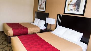 A hotel room with two beds, each with a red and beige bedspread, white pillows, and black headboards. There is a nightstand with a lamp between the beds.