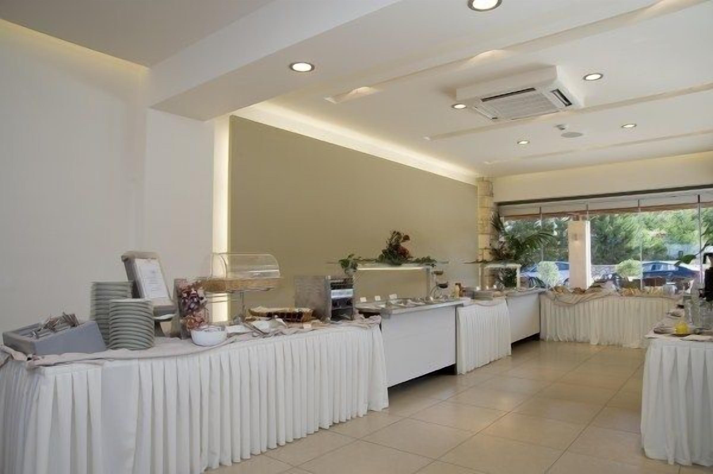 A buffet setup with white tablecloths, a variety of food items, and a large window with a view of the outdoors.