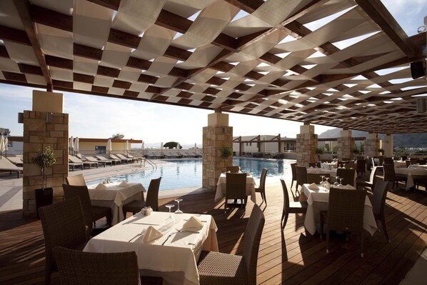 An outdoor dining area with tables and chairs, a pool, and a view of the ocean.