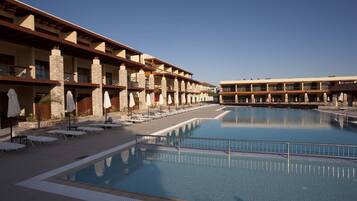 A hotel with a large pool, multiple balconies, and sun loungers.