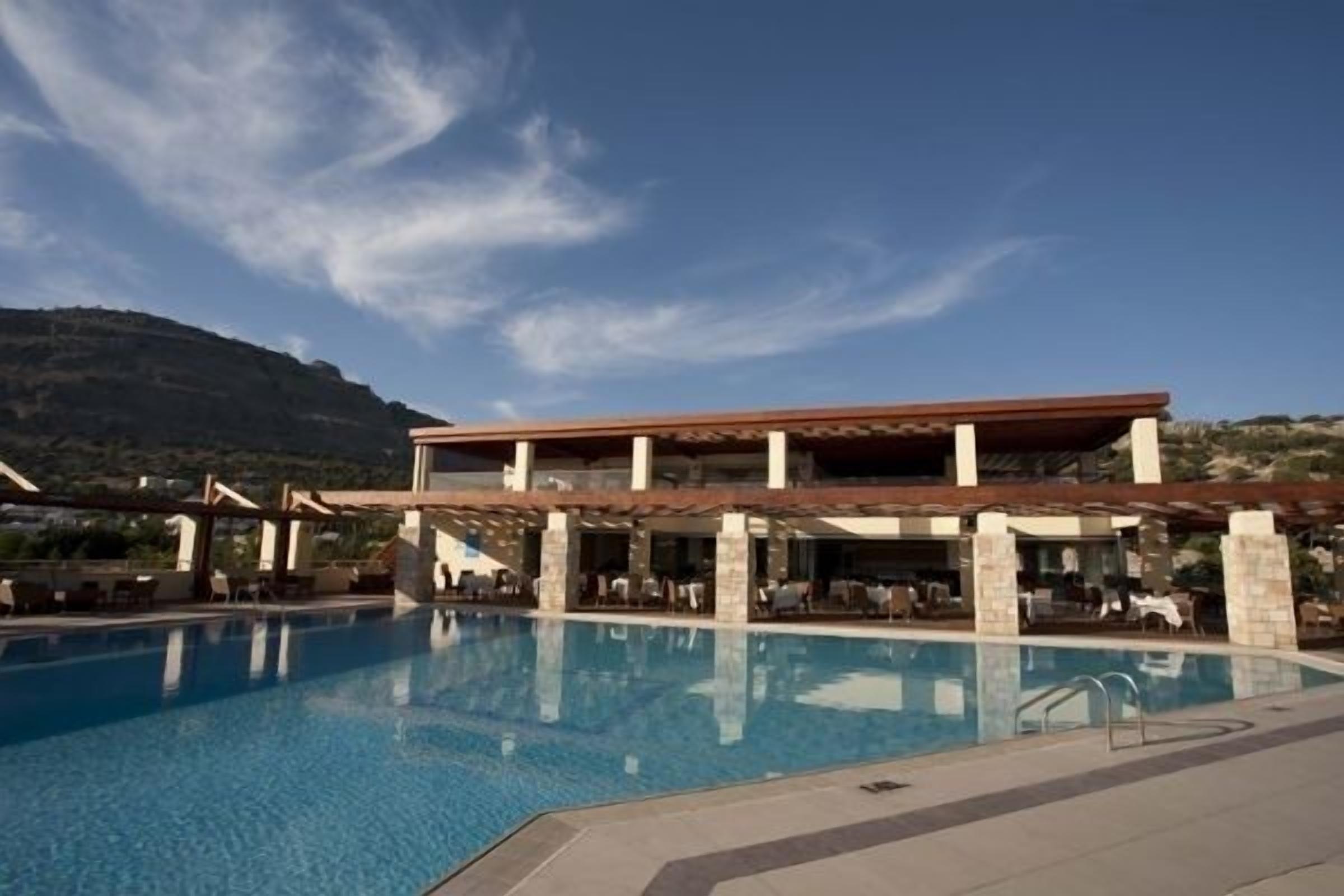 Une piscine entourée d’un bâtiment en arrière-plan, un ciel dégagé et un paysage vallonné.