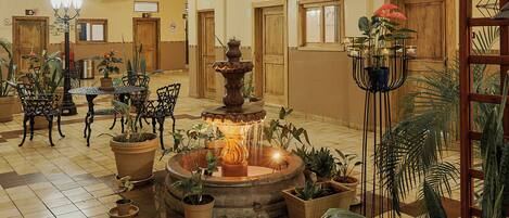 A spacious lobby with a central fountain, multiple potted plants, and a high ceiling with a chandelier.