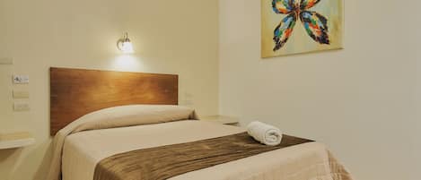 Un lit bien fait, avec une tête de lit en bois, une lampe fixée au mur et un tableau représentant un papillon.