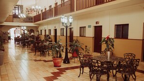 A spacious indoor area with multiple tables and chairs, potted plants, and a balcony. - Hotel Cervantino (Tapachula)