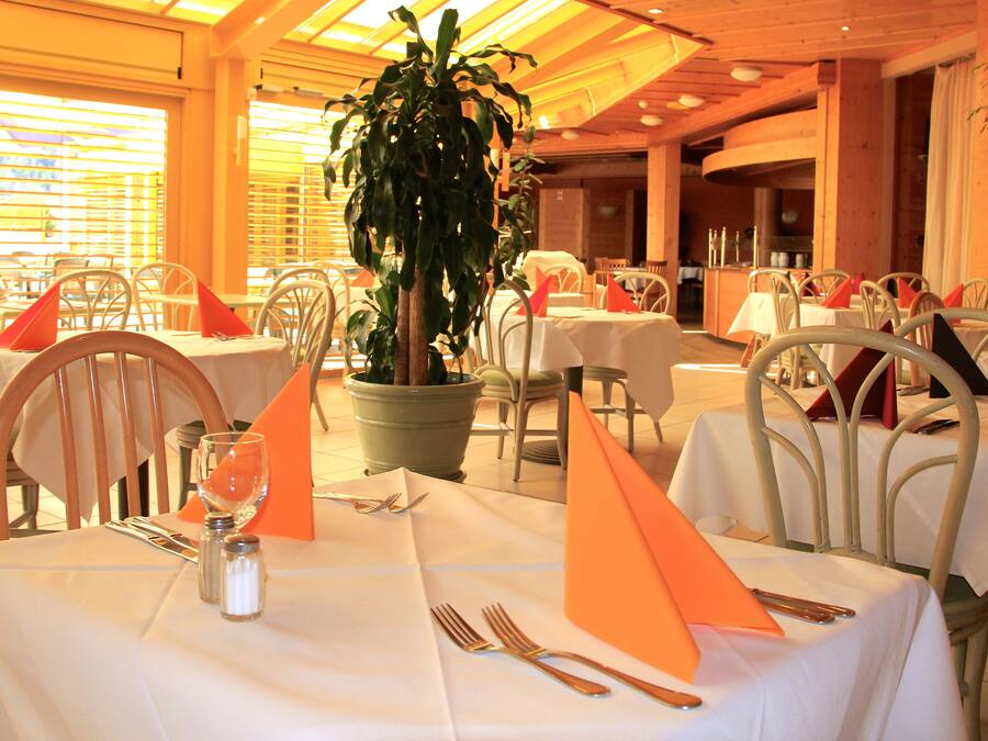 Un restaurante con varias mesas preparadas para comer, con manteles blancos, servilletas anaranjadas y sillas metálicas.