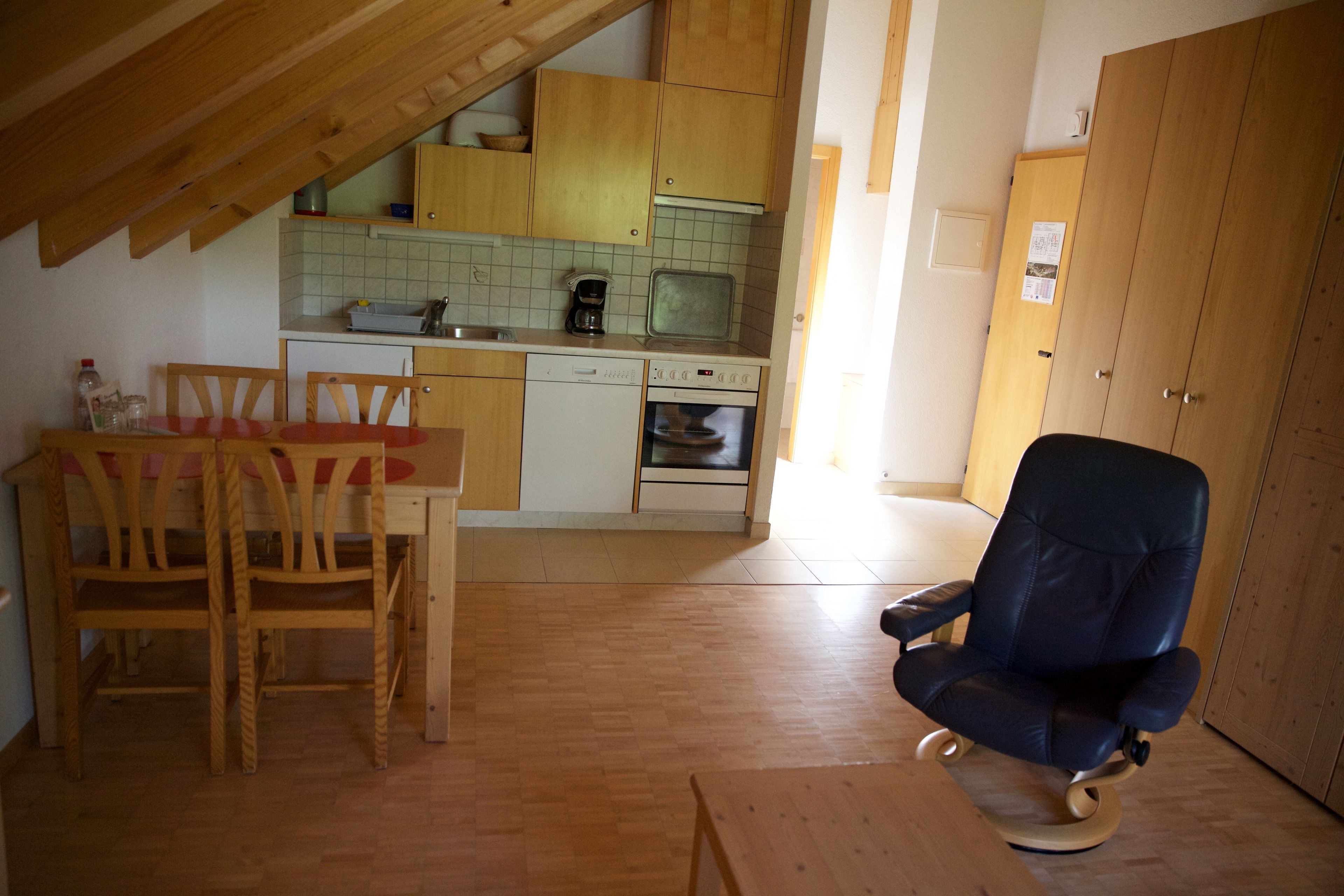 Une cuisine de taille réduite avec des meubles de rangement en bois, une table à manger avec des chaises et un fauteuil à bascule.