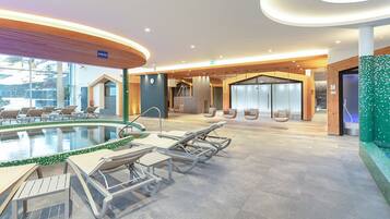 Ein moderner Poolbereich mit Liegestühlen und einem durch eine Glaswand abgetrennten Wellnessraum.