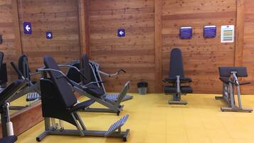 Une salle de sport équipée de matériel d’exercice, avec des murs en bois et une signalétique directionnelle.
