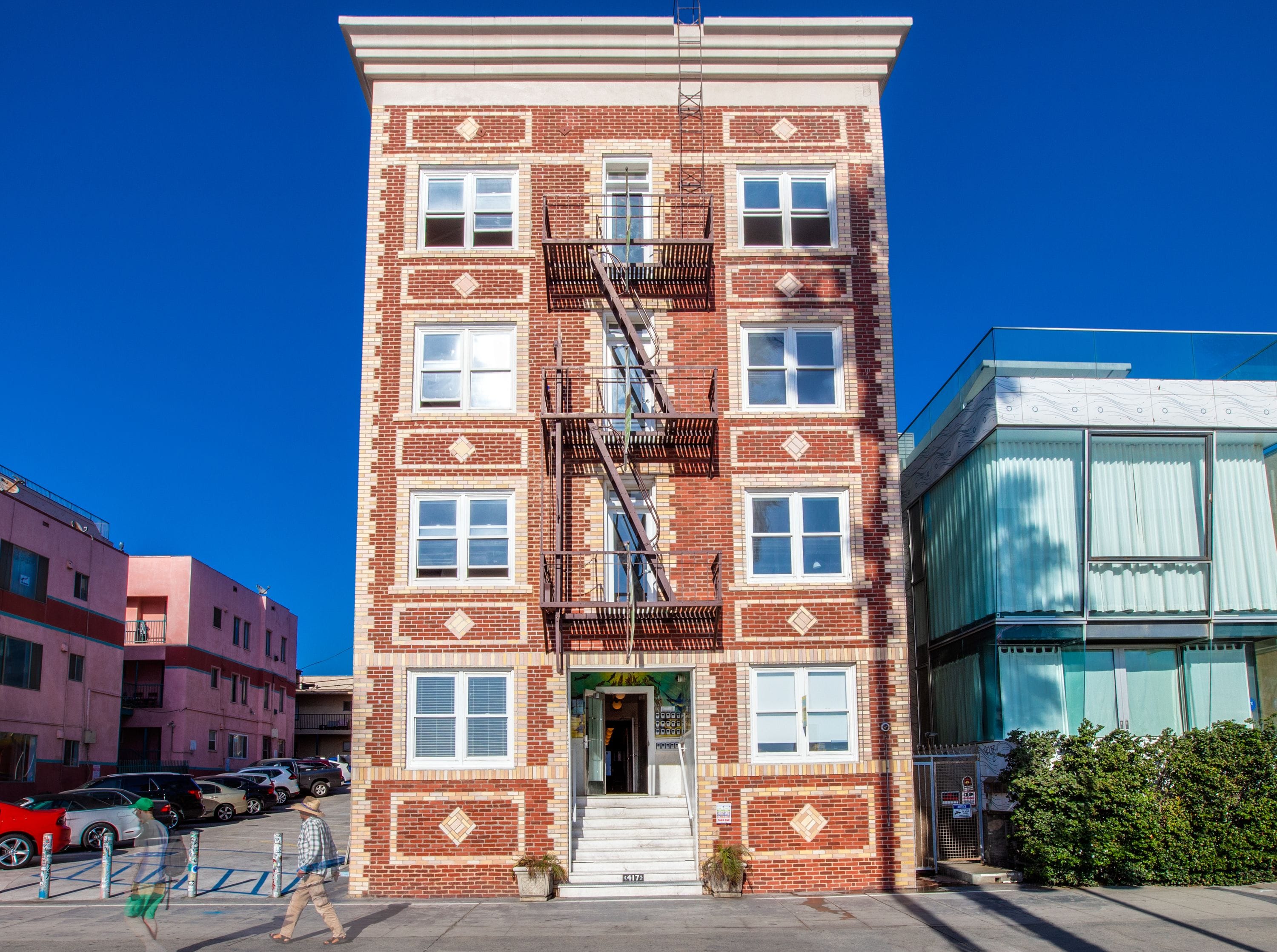 A multi-story brick building with a fire escape, a gated entrance, and a visible storefront.