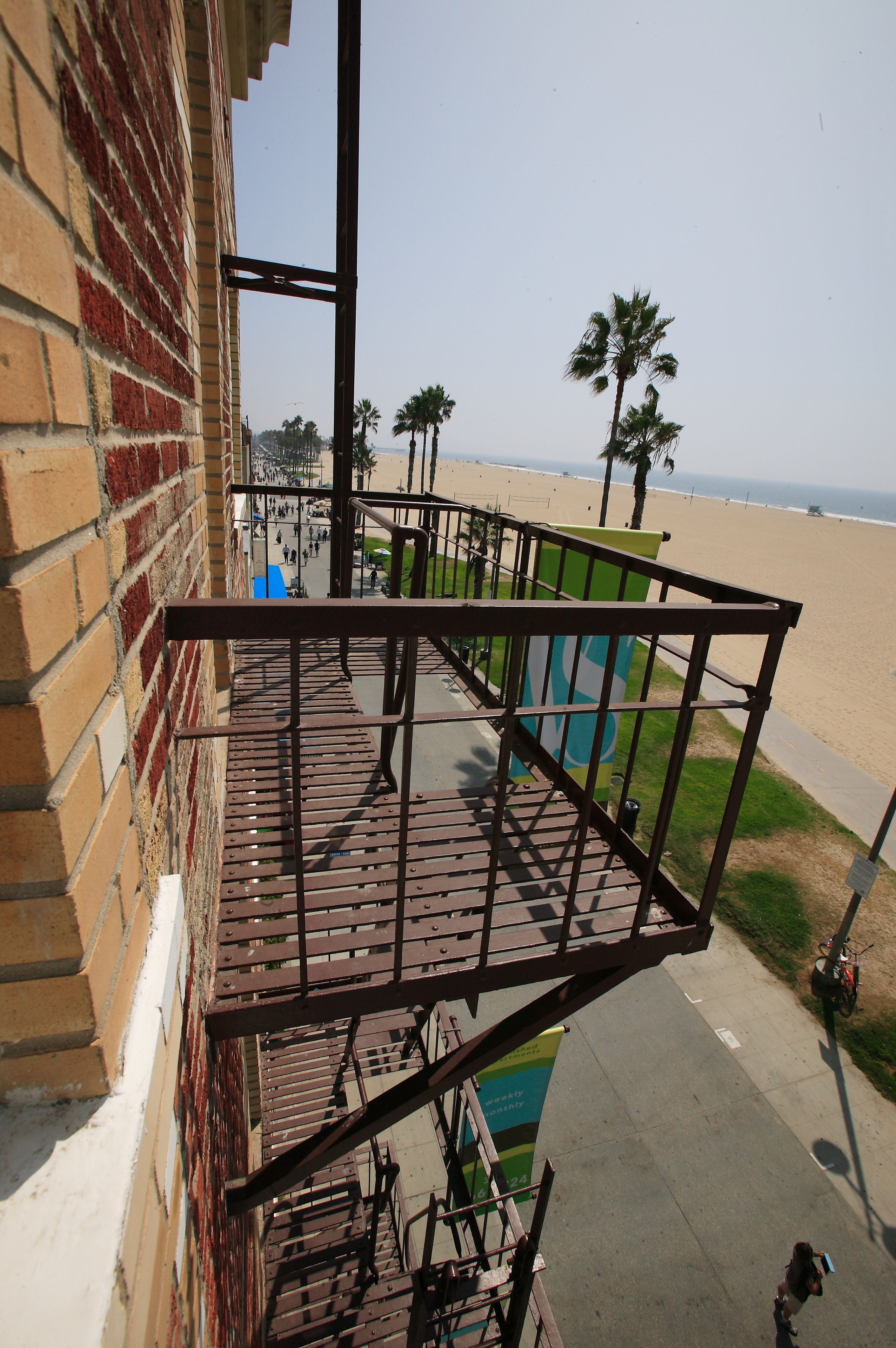 A balcony with a metal railing overlooking a beach with palm trees and a clear sky.