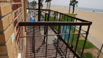 A balcony with a metal railing overlooking a beach with palm trees and a clear sky.
