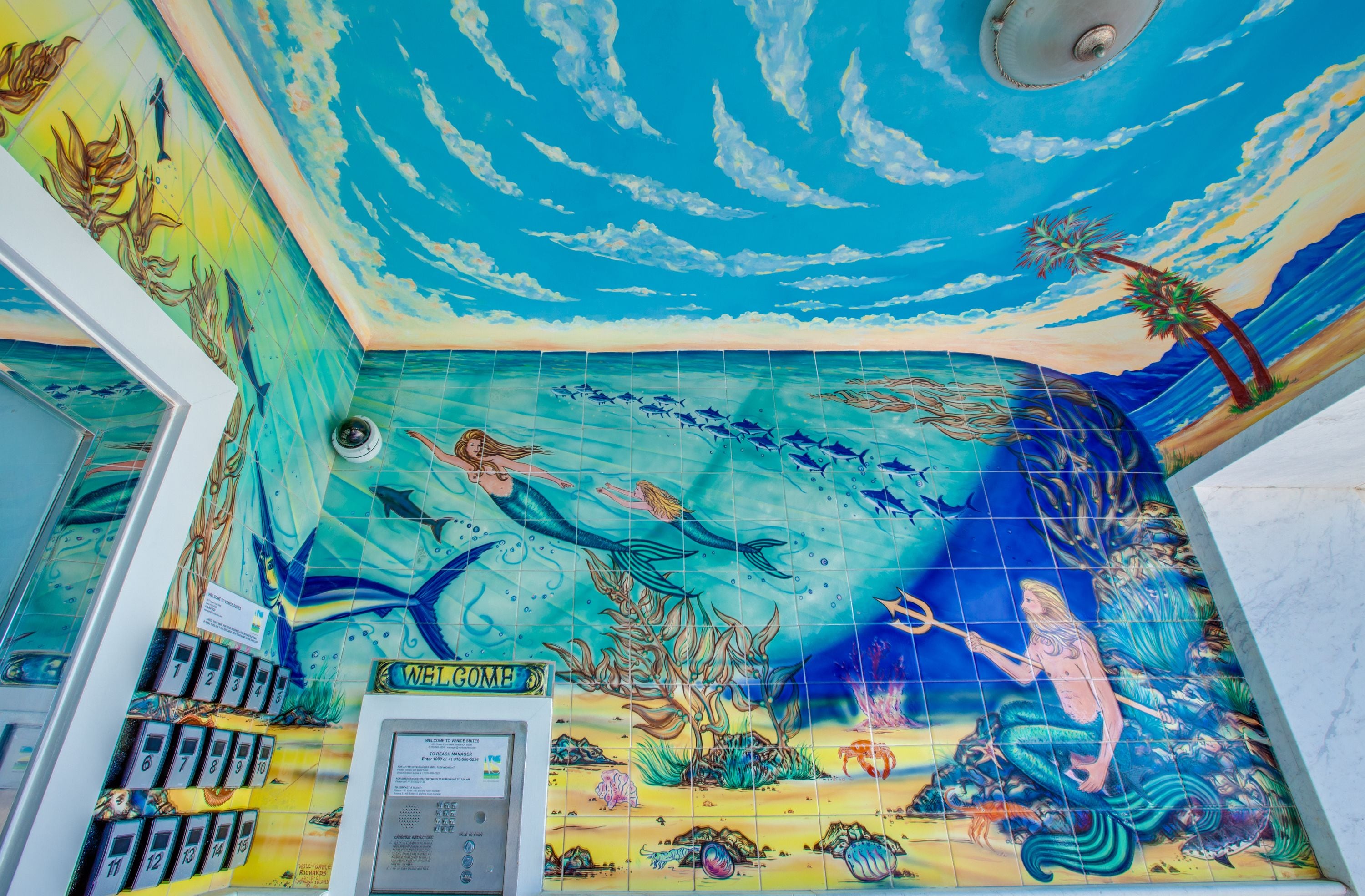 Et værelse med et levende muralmaleri af en undervandsverden, inklusive havfruer og havdyr.