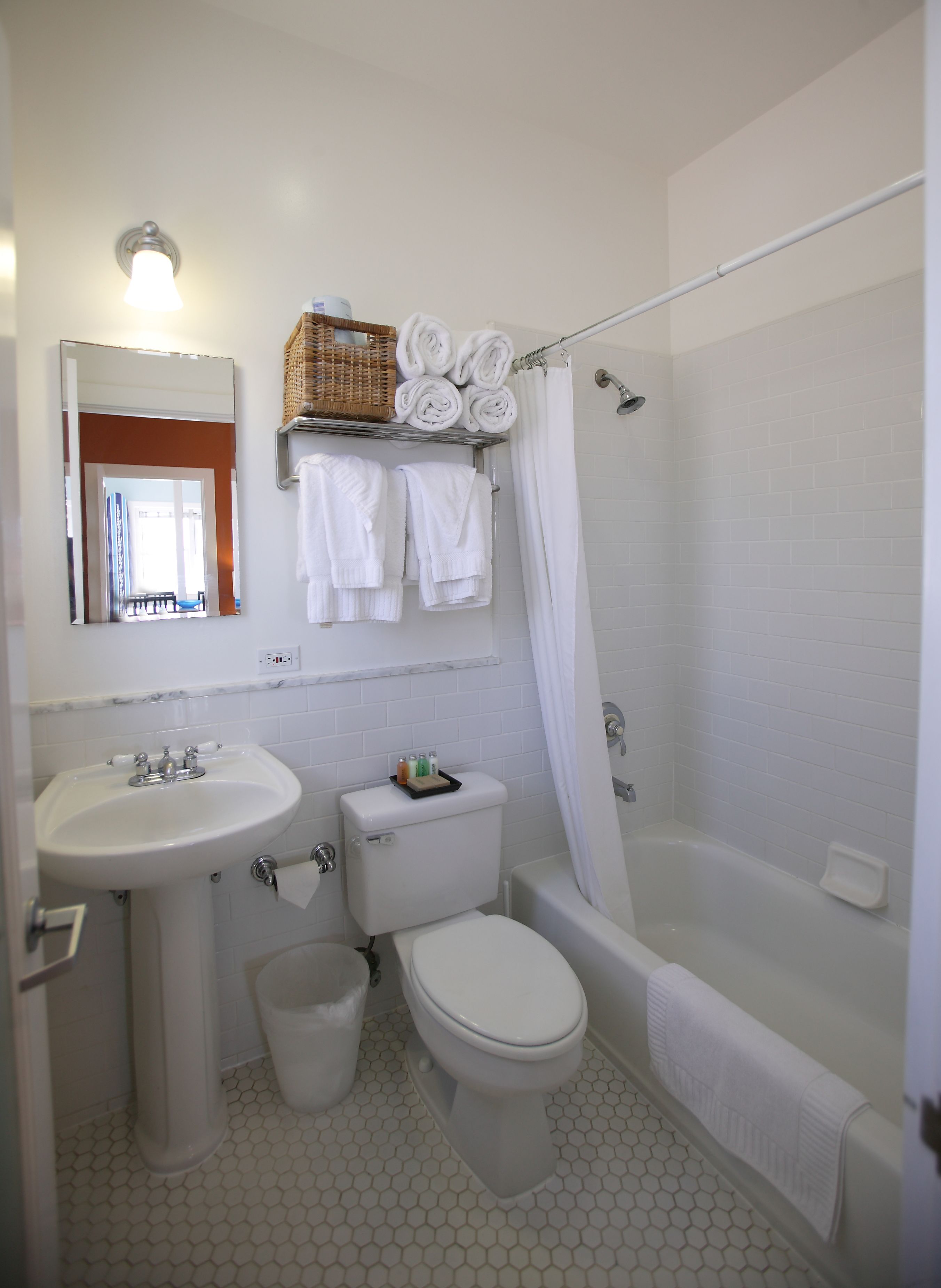 Een badkamer met een wastafel, toilet en bad. Boven de wastafel hangt een spiegel en handdoeken zijn aan de muur opgehangen.