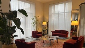 A living room with red chairs, a coffee table, and a large plant. - Hotel La Nuova Rotaia (Gallarate)