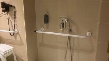 Ein barrierefreies Duschareal mit Haltegriff, weißem Sitzhocker und Bedienfeld an der Wand.