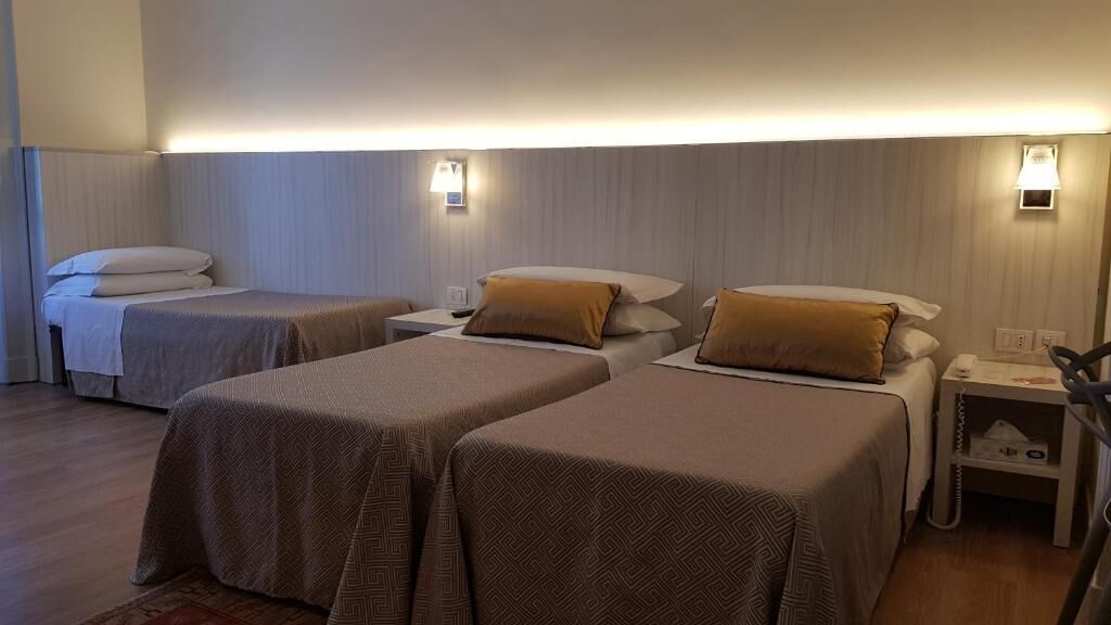 A hotel room with two single beds, each with a bedside table and lamp.