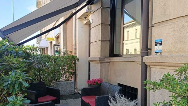 A rooftop patio with outdoor seating, a building with a sign, and a clear sky. - Hotel La Nuova Rotaia (Gallarate)