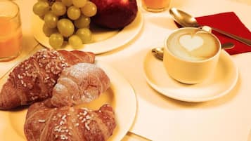 A breakfast setting with croissants, grapes, an apple, and a cup of coffee with a heart design on the foam.