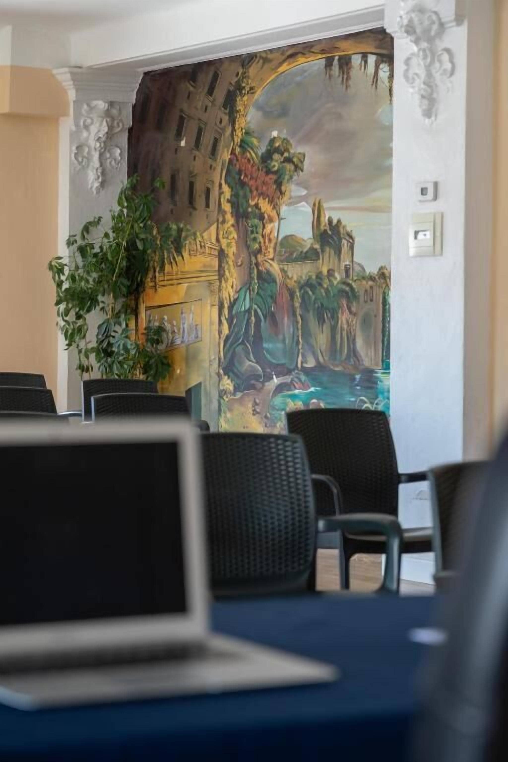 Una habitación con una laptop sobre una mesa, una planta y un mural en la pared.