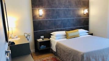 A hotel room with a bed, bedside tables, a nightstand, a lamp, and a decorative rug.
