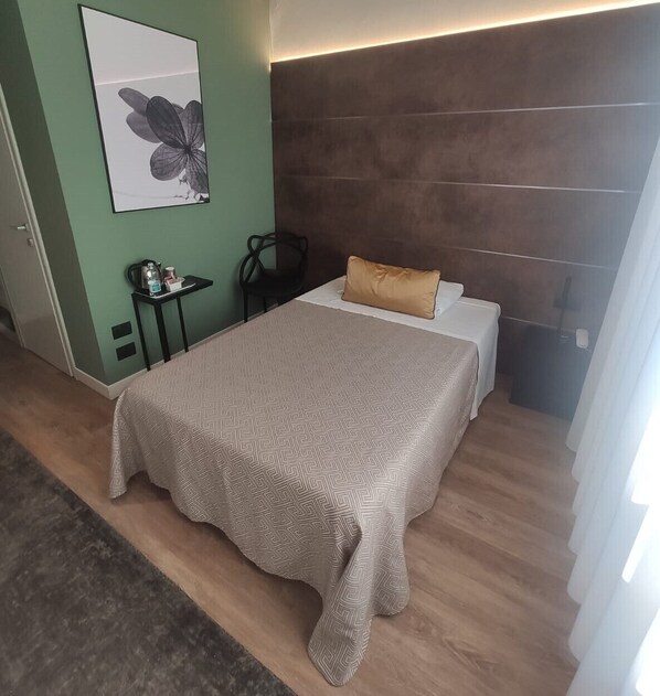Quarto com cama, mesa de cabeceira, cadeira e obra de arte na parede.