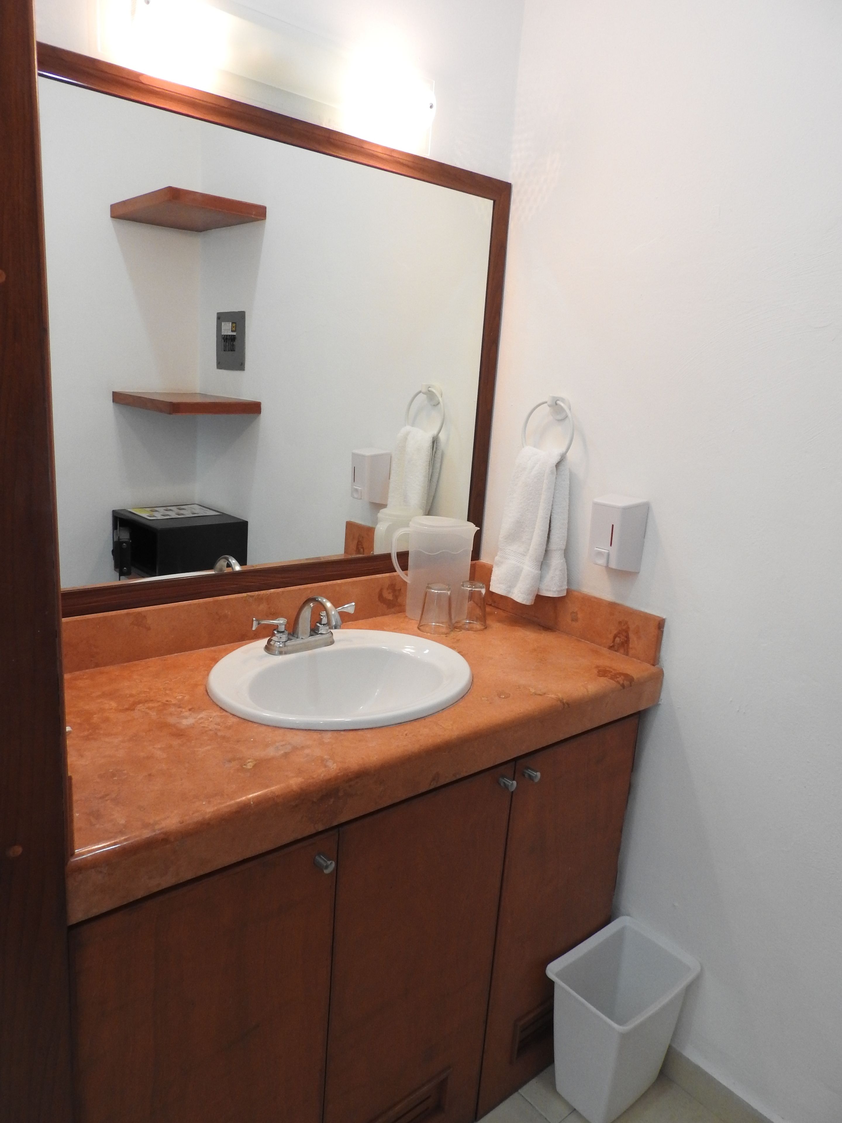 A bathroom with a sink, mirror, towel rack, and a trash bin.