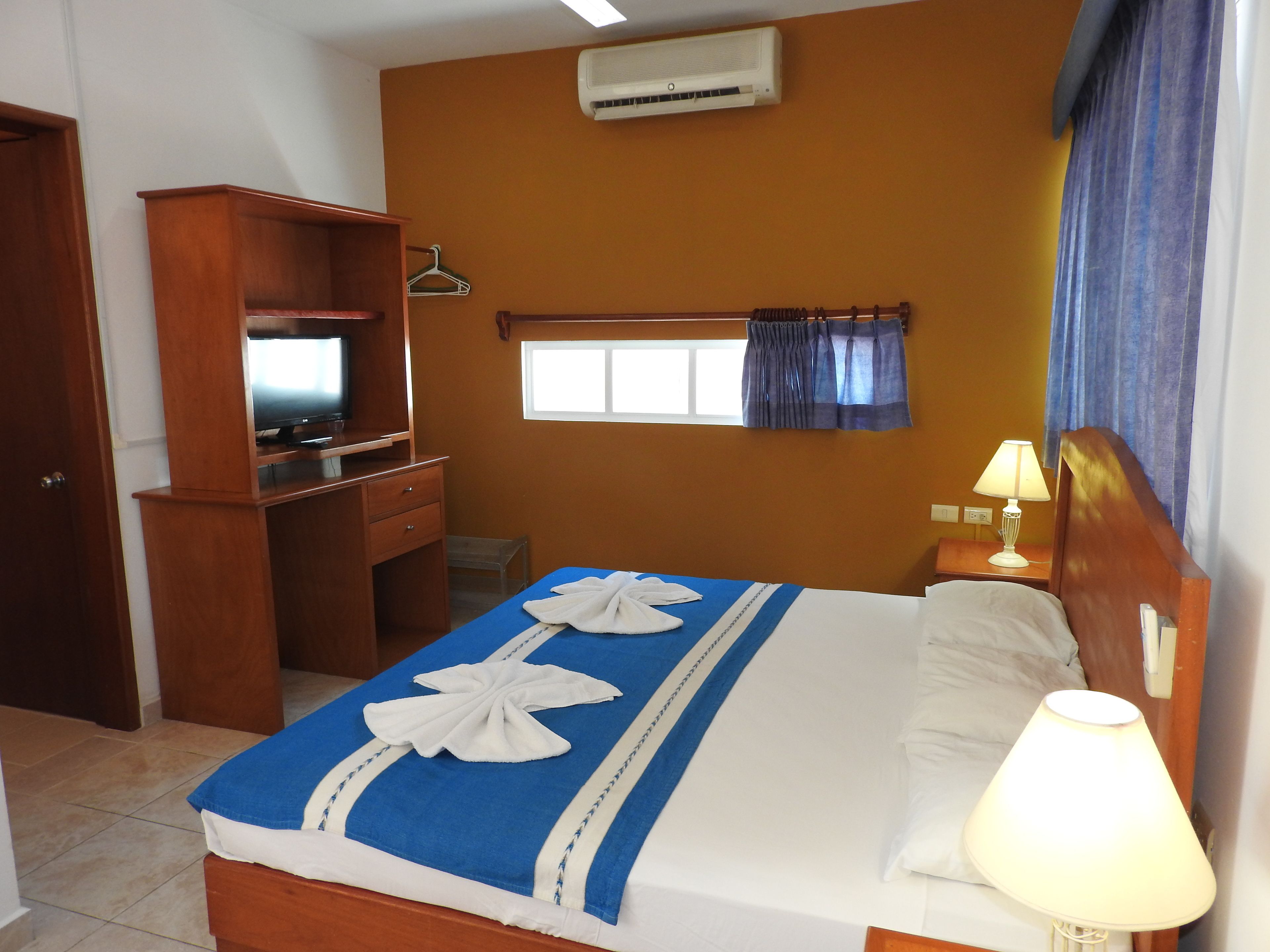 A hotel room with a bed, a desk, a television, an air conditioner, and a window with curtains.