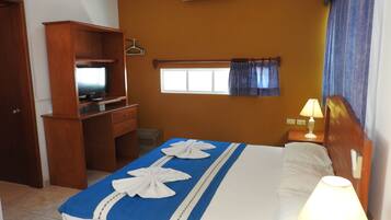 A hotel room with a bed, a desk, a television, an air conditioner, and a window with curtains.