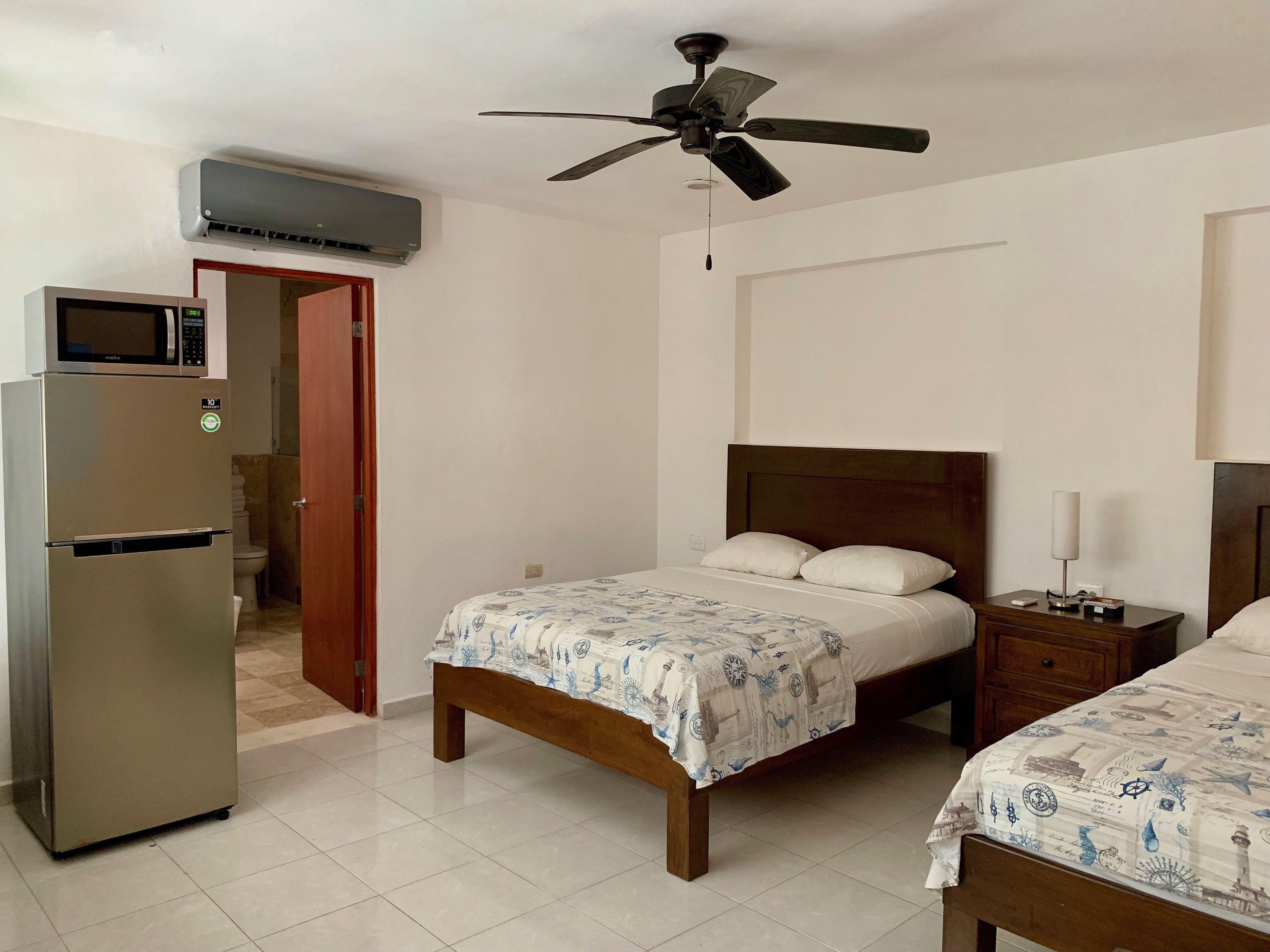 A hotel room with a bed, a nightstand, a microwave, and a refrigerator.