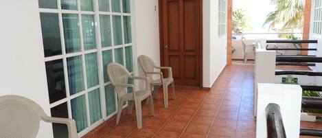 A corridor with a wooden door, a window with frosted glass, and two plastic chairs.