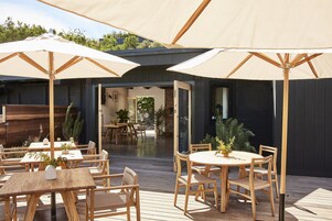 Una terrazza esterna con tavoli e sedie in legno, grandi ombrelloni e vasi con piante.