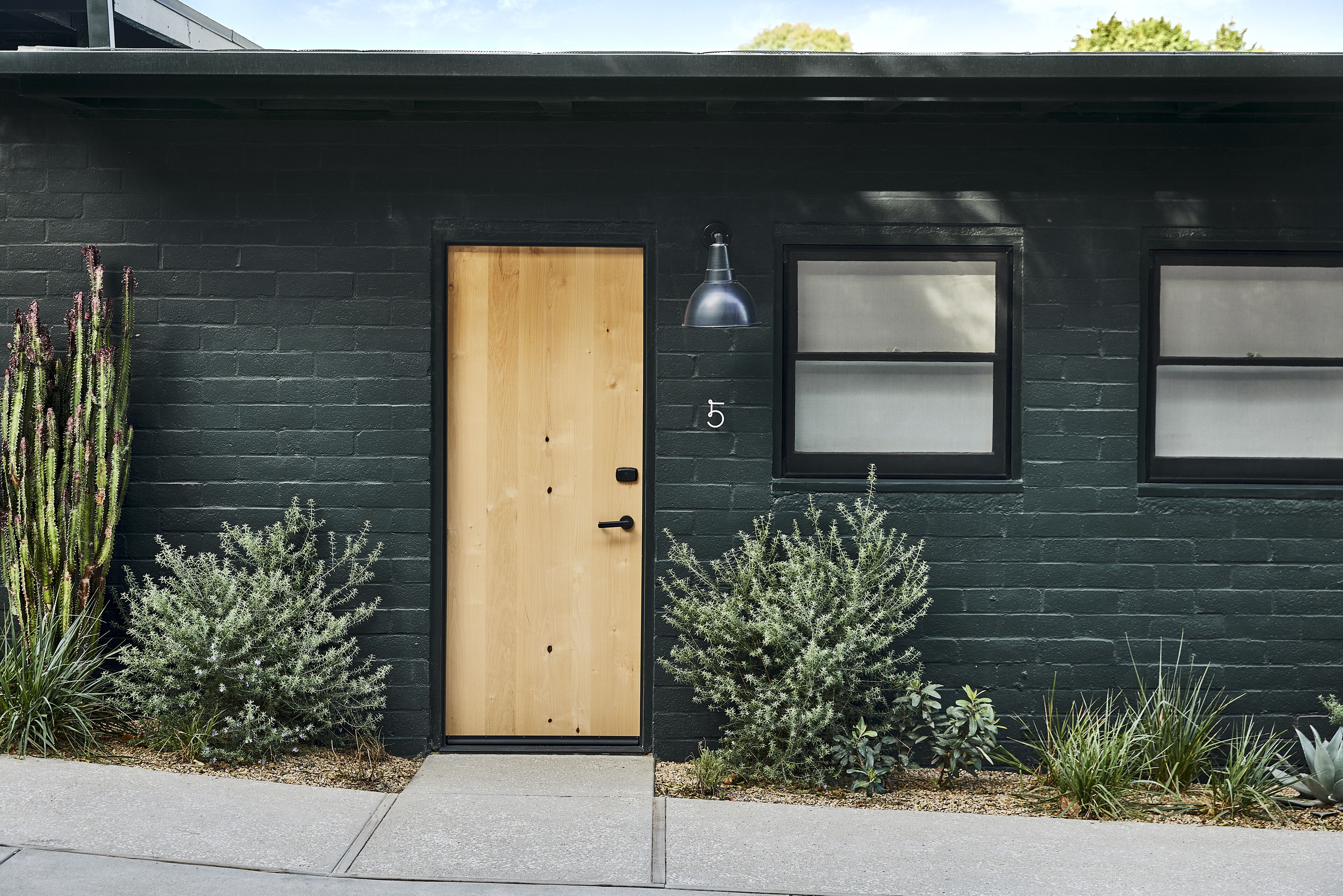 Une maison moderne à l’extérieur sombre, avec une porte d’entrée en bois et un petit porche.