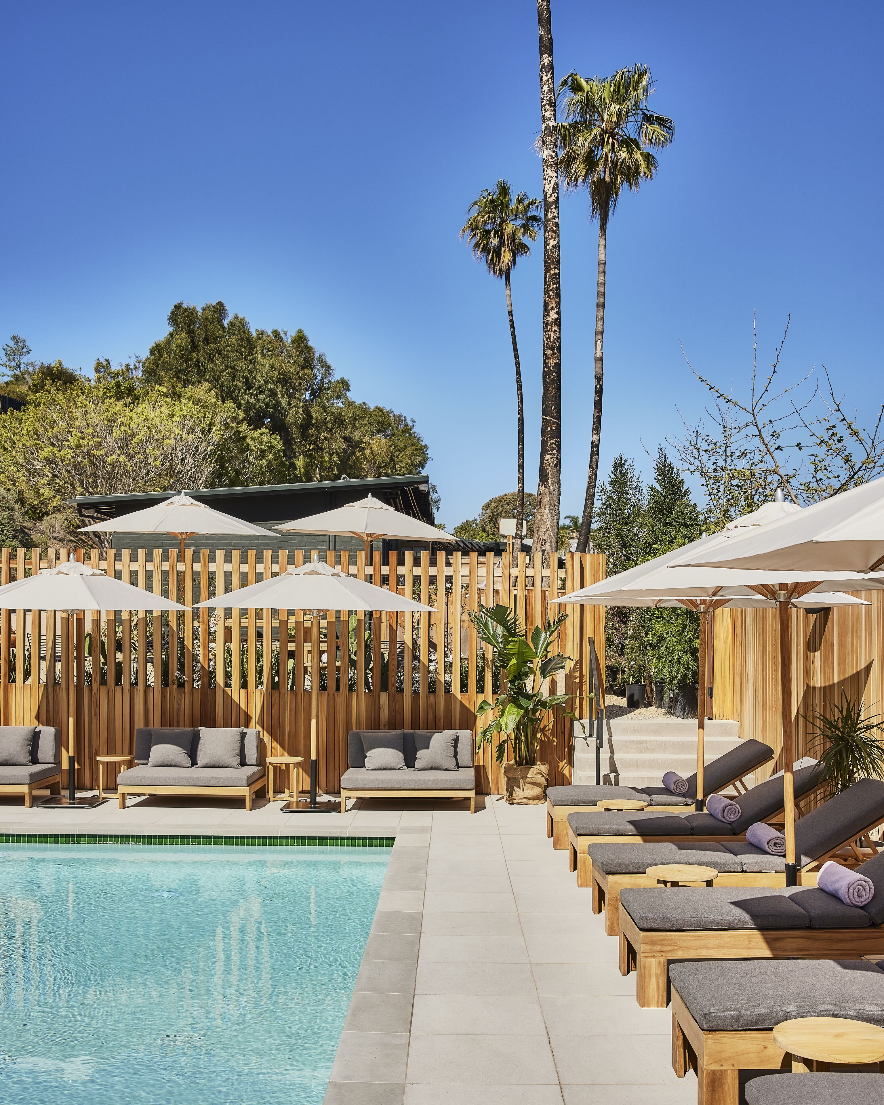 Zona junto a la piscina con sillones de descanso, sombrillas y una valla de madera.