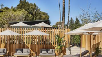 Zona junto a la piscina con sillones de descanso, sombrillas y una valla de madera.