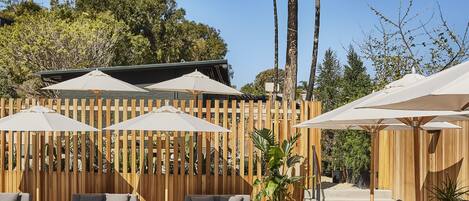 A poolside area with lounge chairs, umbrellas, and a wooden fence.