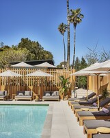 Zona junto a la piscina con sillones de descanso, sombrillas y una valla de madera.