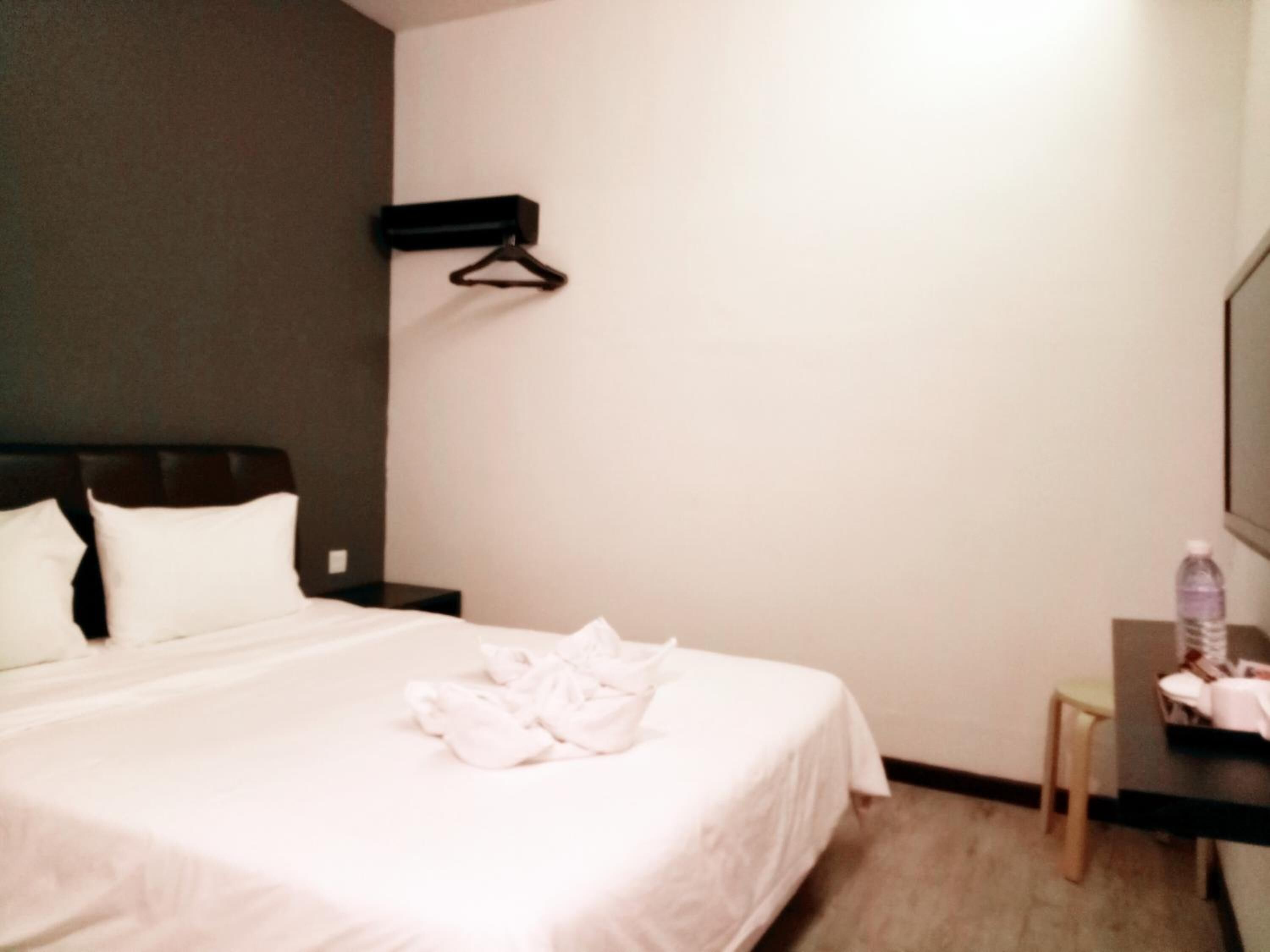 A hotel room with a bed, a nightstand, a desk with a chair, and a hanging coat rack.