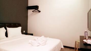 A hotel room with a bed, a nightstand, a desk with a chair, and a hanging coat rack.