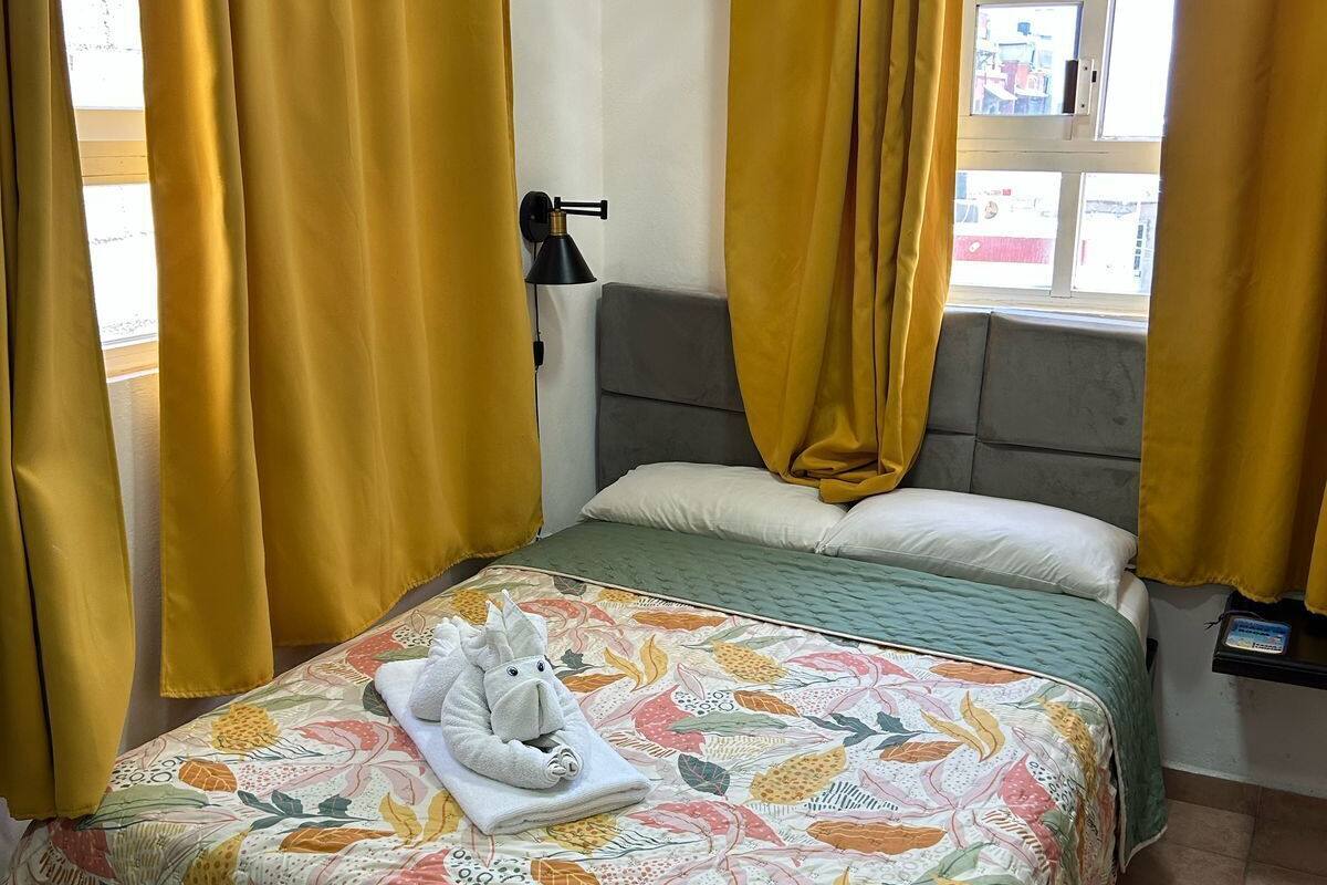A bed with a floral bedspread, a plush toy, and yellow curtains.