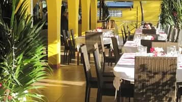 Un espace de restauration en plein air, avec des tables et des chaises, entouré de murs jaunes et de plantes en pot.