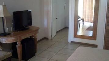 Quarto de hotel com cama, escrivaninha com televisão, espelho e porta que dá para outro cômodo.