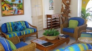 Una sala de estar con un sofá de rayas coloridas, un sillón de mimbre, una mesa de centro con una planta y un estante de pared con adornos.