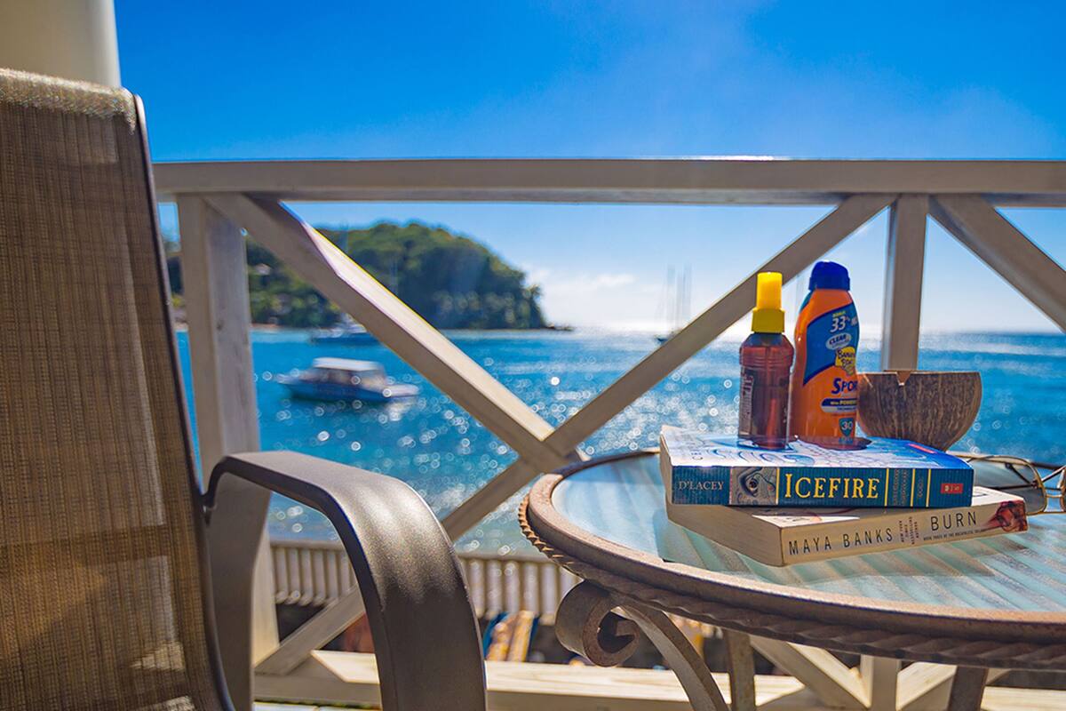 A table with books and sunscreen bottles on a balcony overlooking a body of water.