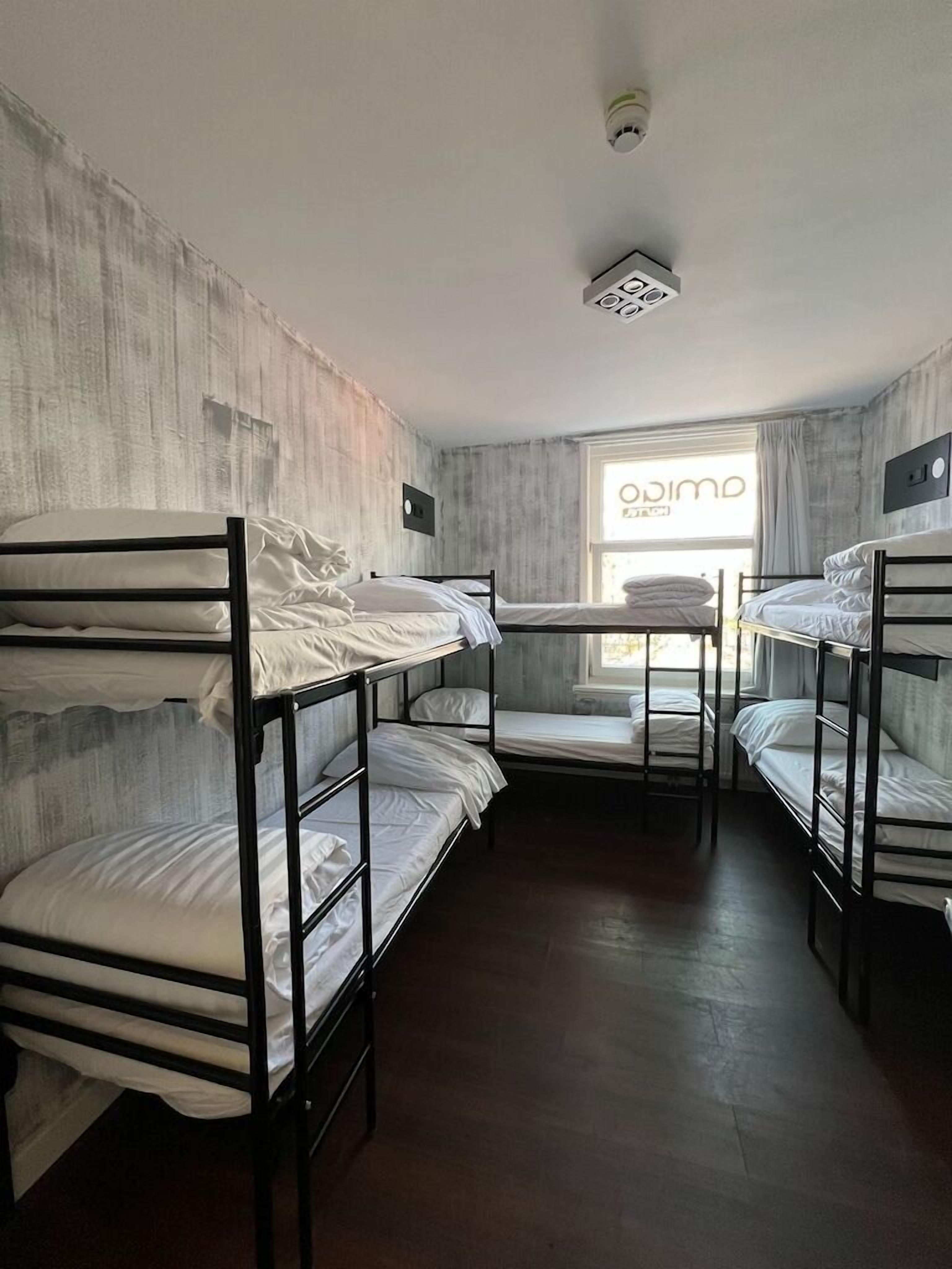 A dormitory room with bunk beds, a window with curtains, and a visible ceiling light fixture.